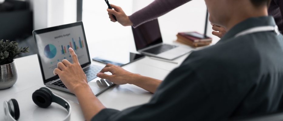 Businesswoman working on laptop computer on office table with person teaching.